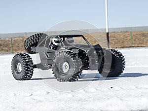 Radio controlled car models: a small black buggy toy with dirty splashes stands in the snow.