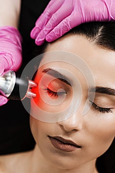 Radio frequency lifting with red light for young woman close-up. Dermatologist is doing radio frequency RF skin