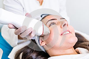 Radio frequency microneedling machine handpiece on the cheek of a woman`s face during a beauty skin tightening treatment photo