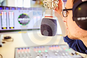 Radio moderator is sitting in a modern broadcasting studio and talking into the microphone