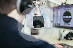 Radio moderator is sitting in a modern broadcasting studio and talking into the microphone