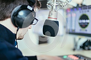 Radio moderator is sitting in a modern broadcasting studio and talking into the microphone