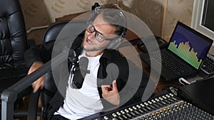 Radio presenter in glasses speaks into microphone beside mixing console