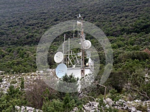 Radio retranslator tower with satellite dish antennas on green hillside