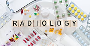 RADIOLOGY word on wooden blocks on a desk. Medical concept with pills, vitamins, stethoscope and syringe on the background