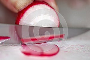 A radish being clipped thinly bu the chef on a cutting board