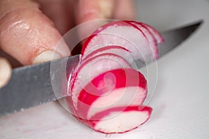 A radish being clipped thinly bu the chef on a cutting board