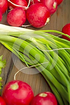 Radish lies next to green onions on a wooden table. Seasonal vegetables in spring. Spring vegetables for salad. Useful