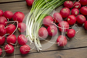 Radish lies next to green onions on a wooden table. Seasonal vegetables in spring. Spring vegetables for salad. Useful