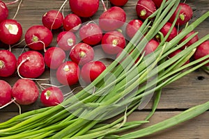 Radish lies next to green onions on a wooden table. Seasonal vegetables in spring. Spring vegetables for salad. Useful