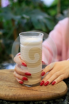 Raf coffee, cappuccino or coffee drink with milk in tall glass cup on wooden board and hands of young woman with red nails. Cafe,