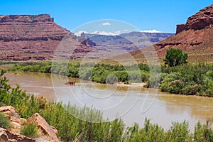 Raft going down Colorado river in Utah desert canyon. La Sal Peak, Mount Waas, Castle Mountain covered in snow on