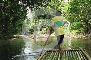 Rafting on bamboo rafts on a mountain river in Khao Lak Park, Thailand. Man controls the raft with a long pole, rear view