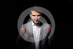 Rage young successful businessman angering over black background.