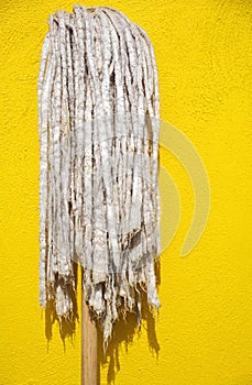Ragged old mop against bright yellow wall