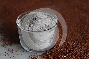Ragi flour in a glass bowl along with a scattered spread of ragi grains around