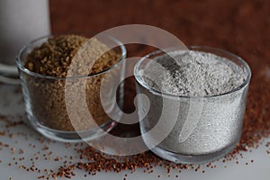 Ragi flour and raw sugar in a glass bowl along with a scattered spread of ragi grains around