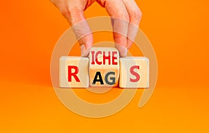 Rags or riches symbol. Concept word Rags Riches on wooden cubes. Beautiful orange table orange background. Businessman hand.