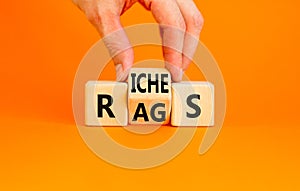 Rags or riches symbol. Concept word Rags Riches on wooden cubes. Beautiful orange table orange background. Businessman hand.