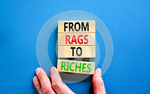 Rags or riches symbol. Concept words From rags to riches on wooden blocks. Beautiful blue table blue background. Businessman hand