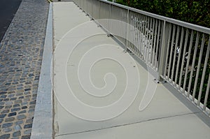 Railing at the bridge with vertical fence bars anchored to the ground with four concrete screws. plastic caps