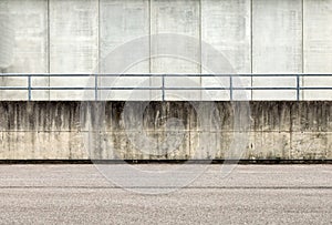 Railing on a grunge concrete wall dividing an asphalt road from a concrete building.