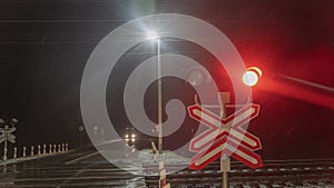 Railroad crossing with passing train by night. Train crossing gates closed on rural road at late evening. Drops of rain