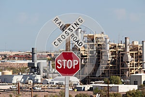 Railroad crossing sign on blue sky and with factory in the back.