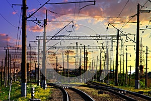 Railroad crossing at station with electric poles on the sunrise cloudy sky background