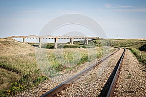 Railroad track running around a curve and under a big concrete bridge.