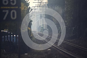 Railroad track with signs and bare trees by the edge of it on a foggy day in autumn