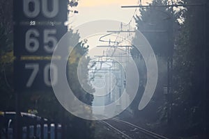 Railroad track with signs and bare trees by the edge of it on a foggy day in autumn