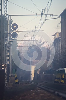 Railroad track with signs and bare trees by the edge of it on a foggy day in autumn