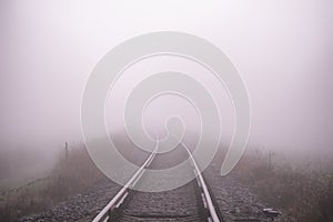 Railroad track in a thick white fog, forest in the background. Concept landscape. Sorrow, loneliness, impasse. Defocused