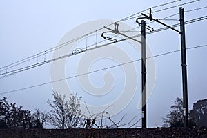 Railroad track on the top of an embankment with bare trees on a misty day in the italian countryside