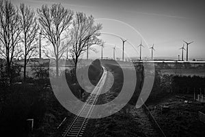 Railroad tracks lead to the horizon where some  wind turbines stand