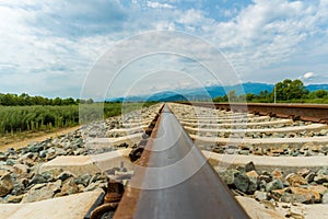 Railroad tracks leading to endless infinity. Meadow landscape and distant mountains.