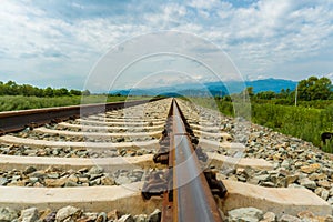 Railroad tracks leading to endless infinity. Meadow landscape and distant mountains.