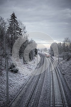 Railroad tracks and red train through snowy trees