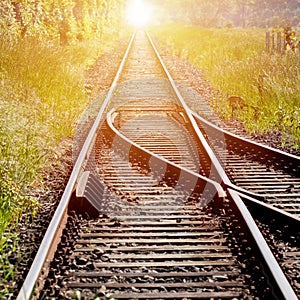 Railroad tracks, with a switch in the foreground, leading to infinity with the red light of the rising sun in the center of the