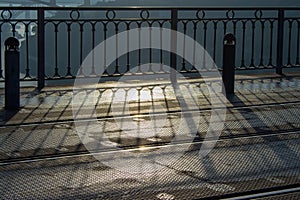 Rails and iron fence in morning light. Modern urban architecture. Shadow from metal fence early in the morning on the street.