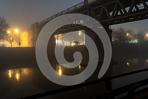 A railway bridge over a river lit up on a foggy, winters night. Worcester, UK