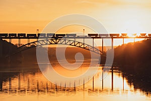 Railway bridge over the river at sunset, a train is moving across the bridge