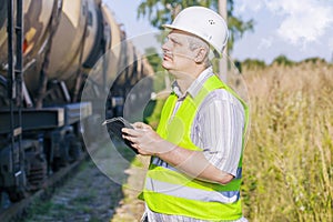 Railway Engineer using tablet PC on railway near freight wagons