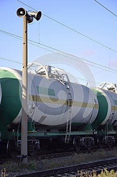 Railway landscape. Many railroad cars and tanks standing in rails. Public address horn loud speakers on wooden pole over blue sk