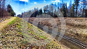 A railway with rails in autumn or spring on a sunny day. Landscape with trees and a slope