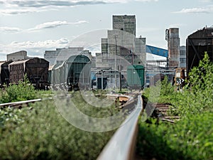 Railway rails extending into the distance to freight cars. In the background are industrial buildings. Sunny summer day