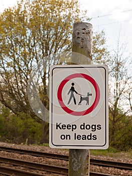 A Railway Safety Sign Saying Keep Dogs on Leads in White and Red