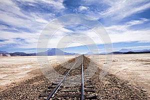 Railway in the salt desert near Uyuni, Bolivia with blue sky and mountains at horizon