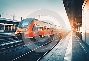 Railway station with beautiful modern red commuter train at suns